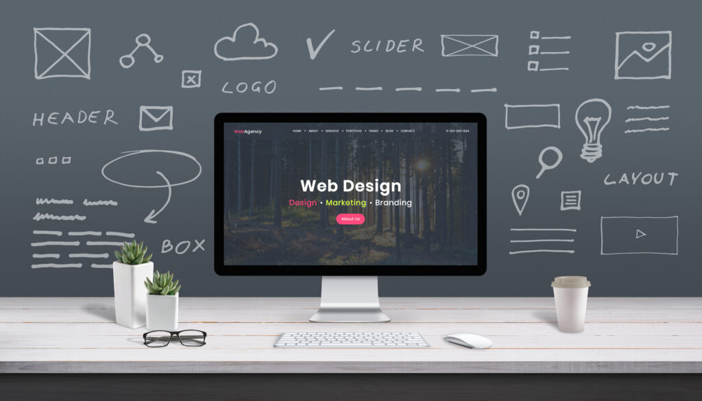 Desktop monitor showing a website design, with layout sketches on the wall behind it